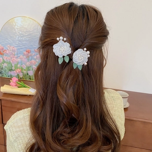 Detailed back view of model wearing white camellia hair clips with pearls and green leaves
