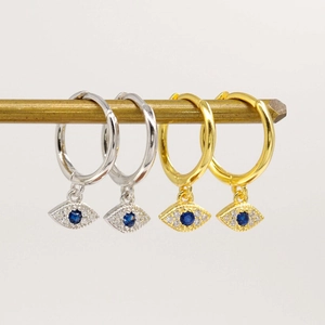 Détail de boucles d'oreilles créoles mauvais œil dorées et argentées avec pierres bleues