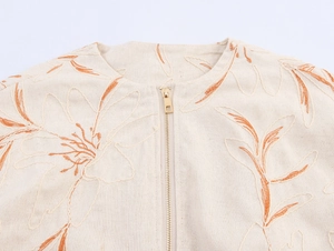 Close-up of orange floral embroidery and golden zipper on beige cotton jacket