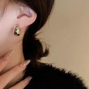 Macro shot of a golden teardrop earring with a high-shine mirror finish on a model