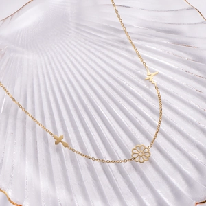 Golden stainless steel necklace featuring cross, heartbeat, and flower charms on shell tray