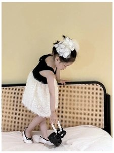 Girl wearing black dress with white fringe hem and holding a mini pearl handle handbag