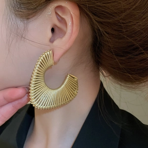 Detailed close-up of large golden C-shaped textured earrings on a fashion model