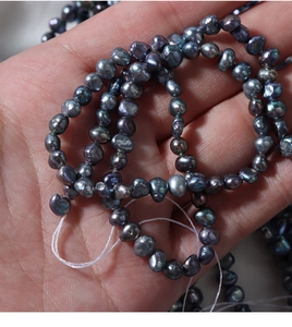 Macro shot of 4-5mm baroque freshwater pearls with peacock metallic luster on hand