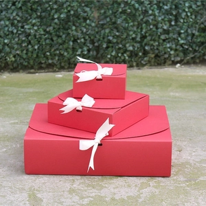 Three-piece red square gift box set with white ribbons in an outdoor natural setting