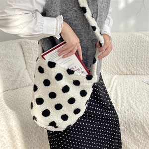 Close-up of white plush shoulder bag with black polka dots on a soft neutral background