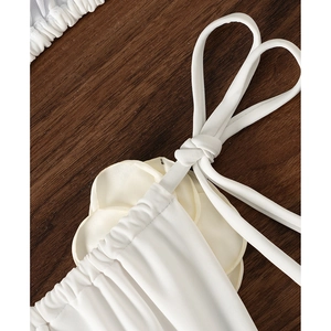 Detailed view of white bikini top with 3D fabric flowers and thin straps on wood