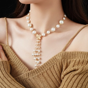 Detail of faux pearl flower tassel necklace with golden clover on brown sweater