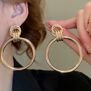 Minimalistische große goldene Creolen mit Dreifach-Ring-Verbindung an einem weiblichen Model
