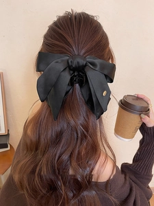 Rear view of model wearing a black satin bow hair claw with gold detail in a cozy indoor setting