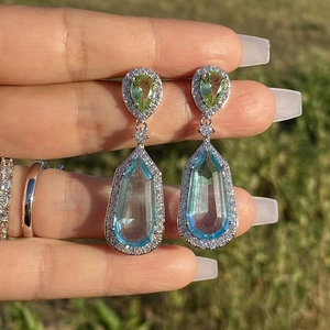 Detail of drop earrings featuring pear-cut green and blue crystals with pave halo