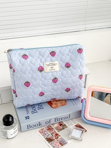 Close-up of strawberry print on blue striped quilted makeup bag with heart stitching