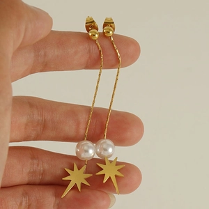 Detail of star-shaped pearl drop earrings with long gold tassel chains worn on model