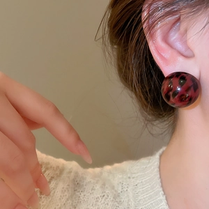 Close-up of leopard print resin dome stud earring on model with white sweater background