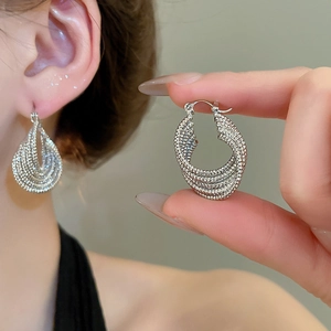 Detailed view of silver multi-layer braided twist hoop earrings on model and hand