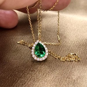 Detailed close-up of emerald pear-shaped pendant with diamond halo and 18K gold chain