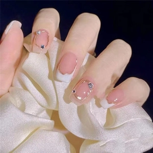 Close-up of pink french tip press-on nails with golden frames and sparkling rhinestones