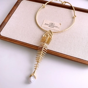 Macro shot of gold fishbone necklace with rhinestones and drop pearl on a wooden tray