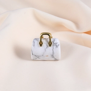 Detail of a white marble handbag pendant with a gold metal handle on beige fabric