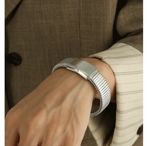 Close-up of wide ribbed silver stainless steel cuff bracelet worn with a checkered blazer