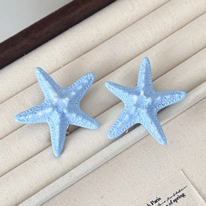 Pair of light blue starfish stud earrings with realistic textured finish in a jewelry tray