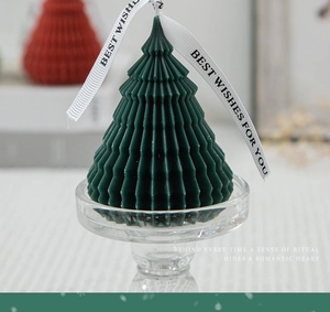 Close-up of a green origami Christmas tree scented candle with ribbon on glass stand