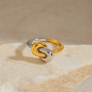 Polished two-tone twisted knot ring in gold and silver on a light stone stand