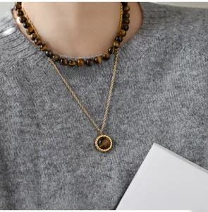 Close-up of layered tiger eye stone bead necklace and gold twisted chain on grey knitwear