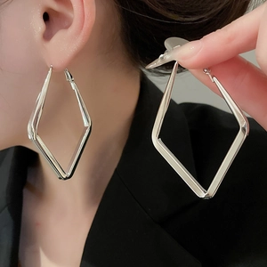 Close-up of oversized silver geometric diamond hoop earrings shown on model and held by hand