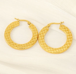 Macro detail of thick gold hoop earrings with embossed star pattern on silk