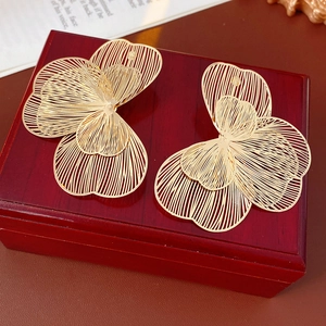 Gros plan sur des boucles d'oreilles pétales dorés posées sur un coffret en bois rouge