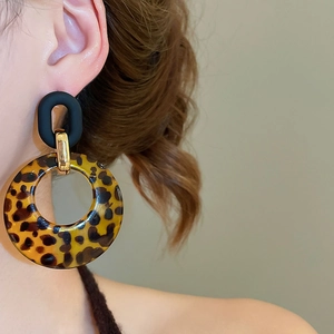 Close-up of a model wearing large leopard print resin earrings with vintage golden clasps