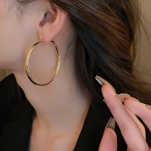 Close-up of a model wearing large minimalist golden geometric hoop earrings with polished finish