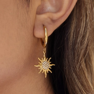 Close-up of a gold sun-shaped earring with small diamonds on a model's ear