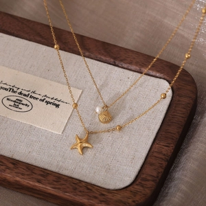 18K gold plated titanium necklace with starfish and shell pendants on linen display