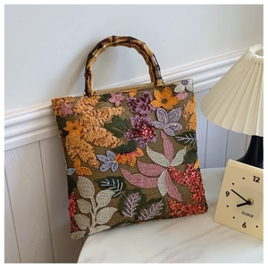 Detail of hand-embroidered floral patterns and bamboo handle on a green linen handbag