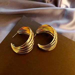Close-up of golden multi-layered geometric C-shaped earrings with textured ridges
