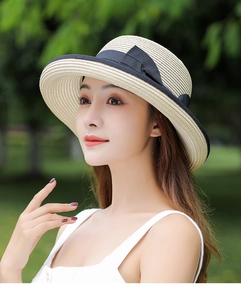 Detailed outdoor view of a beige straw sun hat with a black ribbon bow for women