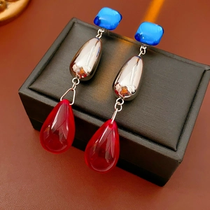 Detailed view of vintage tassel earrings with blue square and red teardrop charms on a box
