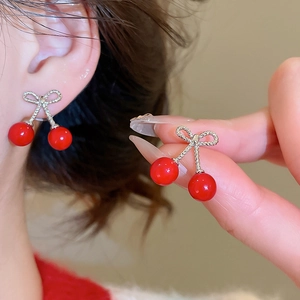 Detailed view of red cherry earrings with silver bowknots worn on an earlobe