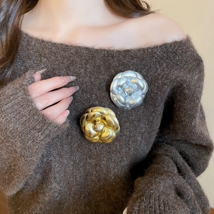 Detail view of gold and silver camellia brooches on a dark brown sweater fabric