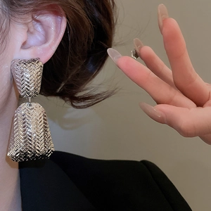 Detailed view of gold geometric earrings with woven texture on a fashion model