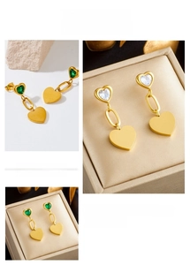 Detail view of heart-shaped gold earrings featuring green and white crystal gemstones