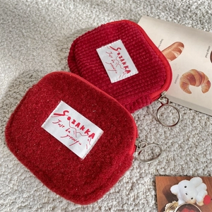 Red plush and corduroy small square wallets with circular metal zippers in cozy setting