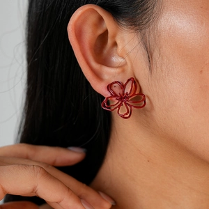Détail macro d'un mannequin portant des boucles d'oreilles fleurs rouges floquées ajourées