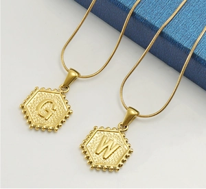 Détail de deux chaînes serpent dorées avec des pendentifs hexagonaux lettres G et W