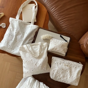 White cotton tote and zipper pouches with delicate floral eyelet embroidery on wooden table