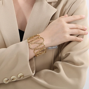 Detail of a wavy layered golden metal cuff bracelet showing its 3D hollow structure