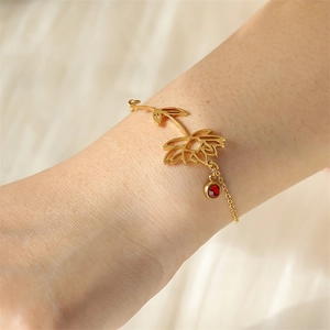 Golden lotus flower bracelet with a red birthstone charm worn on a female wrist
