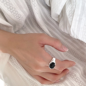 Close-up of fluid silver ring with black onyx stone worn on finger over white fabric